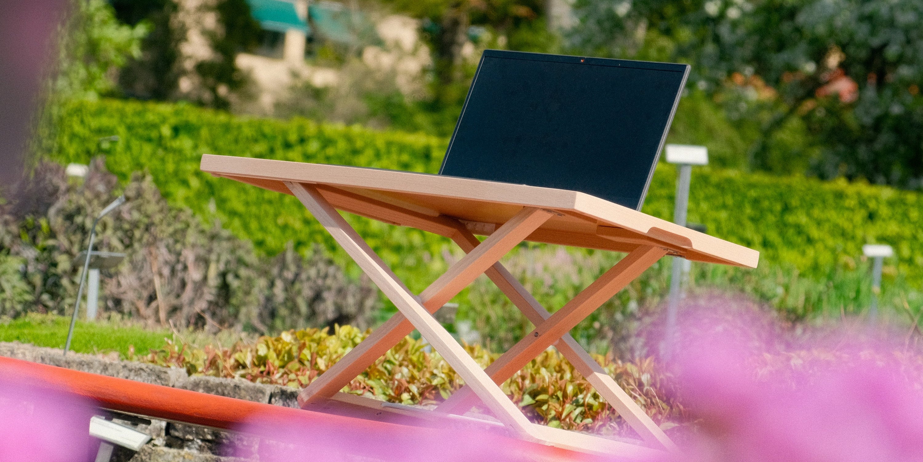 Freedesk Desk riser Light Compact outdoors with flowers framing the image.