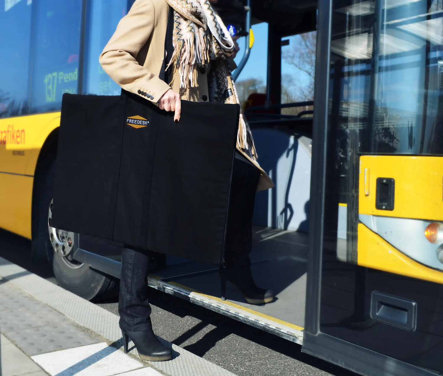 Freedesk Carrying Case Compact in black, designed for convenient transport of the Freedesk Desk Riser, shown being carried outdoors.