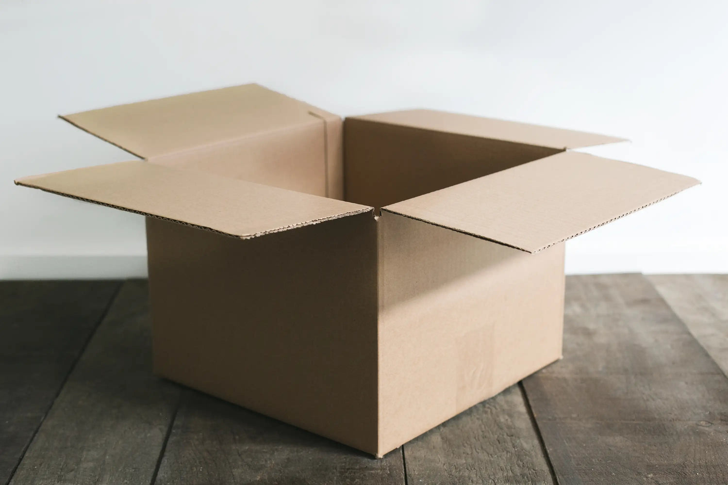 An open cardboard box resting on wooden floor, ready for packing or shipping items.