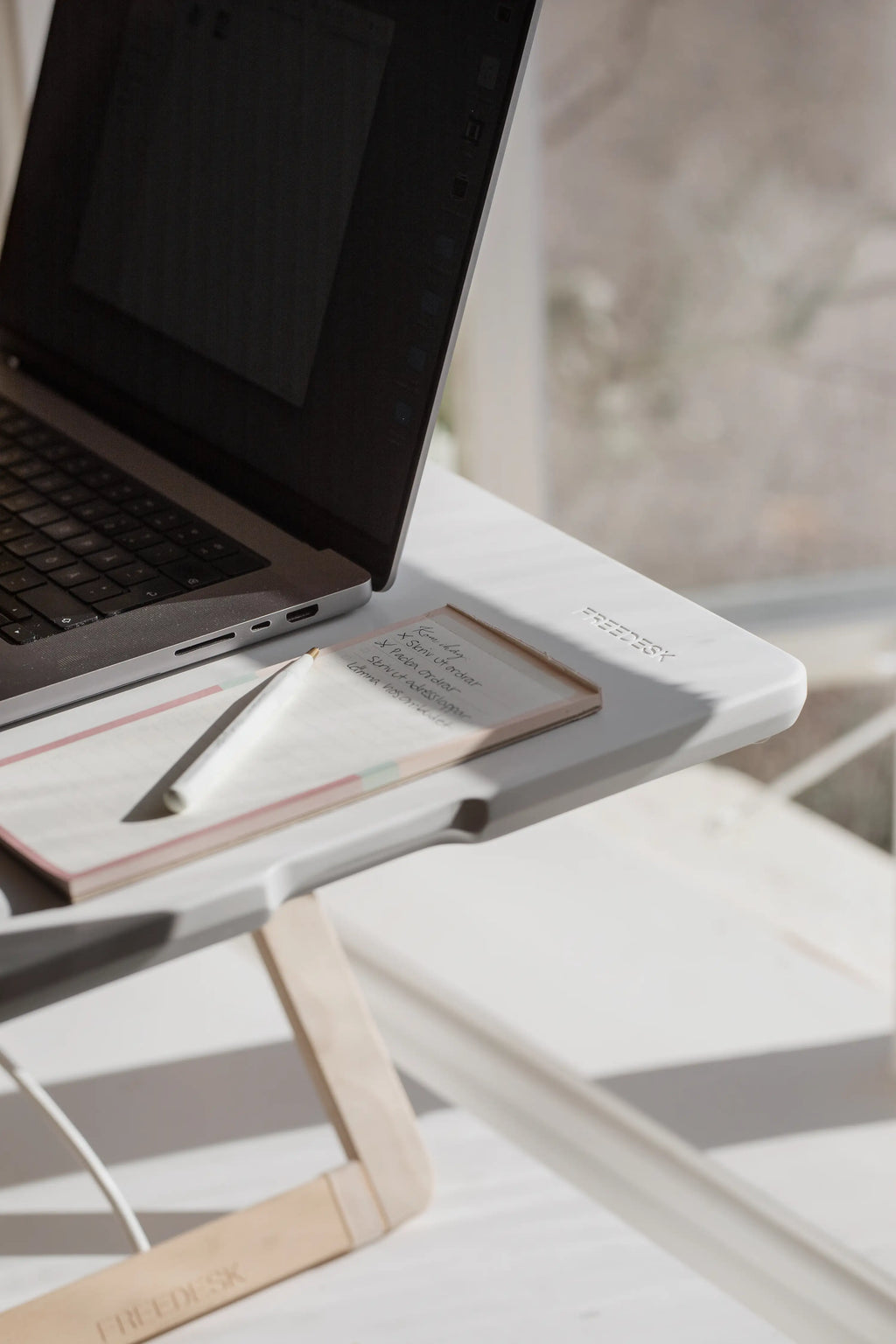 Close-up of Freedesk Desk Riser Original Compact with laptop and notepad in sunlight
