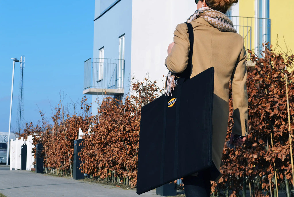 Freedesk Carrying Case Large in black, designed for easy transport of the Freedesk Desk Riser, shown being carried outdoors.