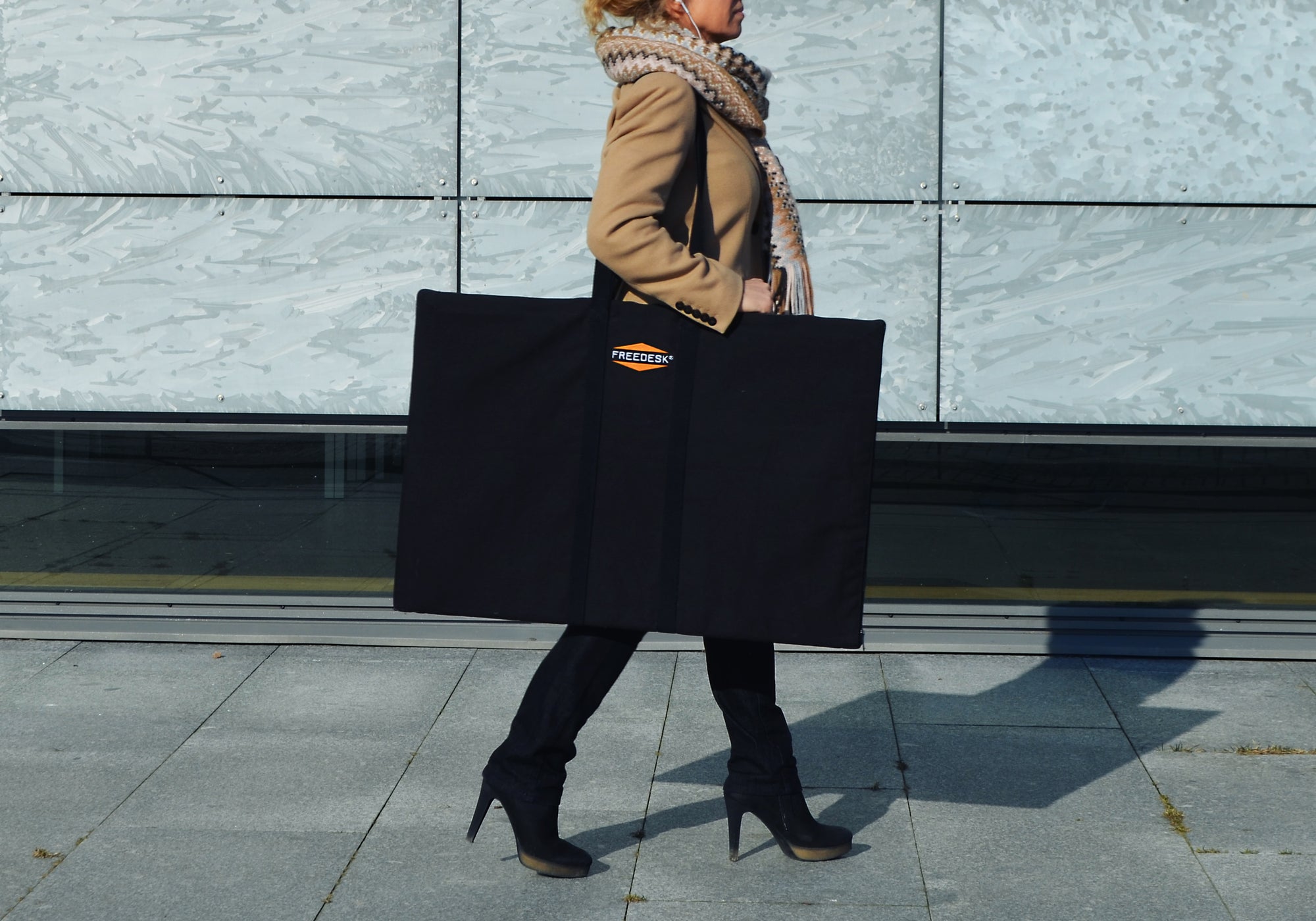Freedesk Carrying Case Compact in black, designed for convenient transport of the Freedesk Desk Riser, shown being carried outdoors.