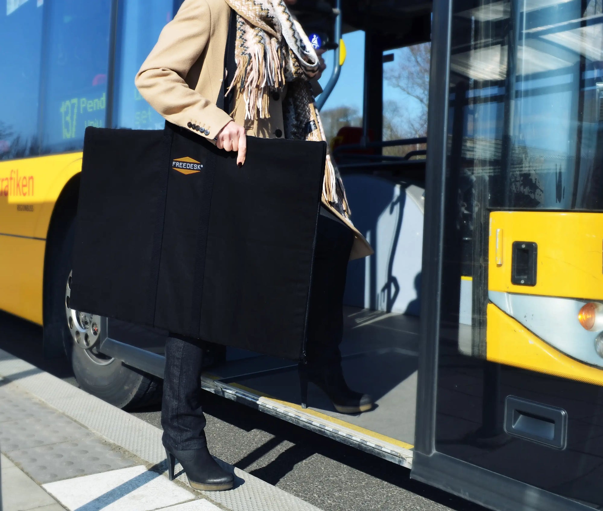 Freedesk Carrying Case Compact in black, designed for convenient transport of the Freedesk Desk Riser, shown being carried outdoors.