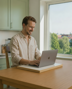Man sitting down and working comfortably with a laptop on a portable height & adjustable desk riser in a home office setting