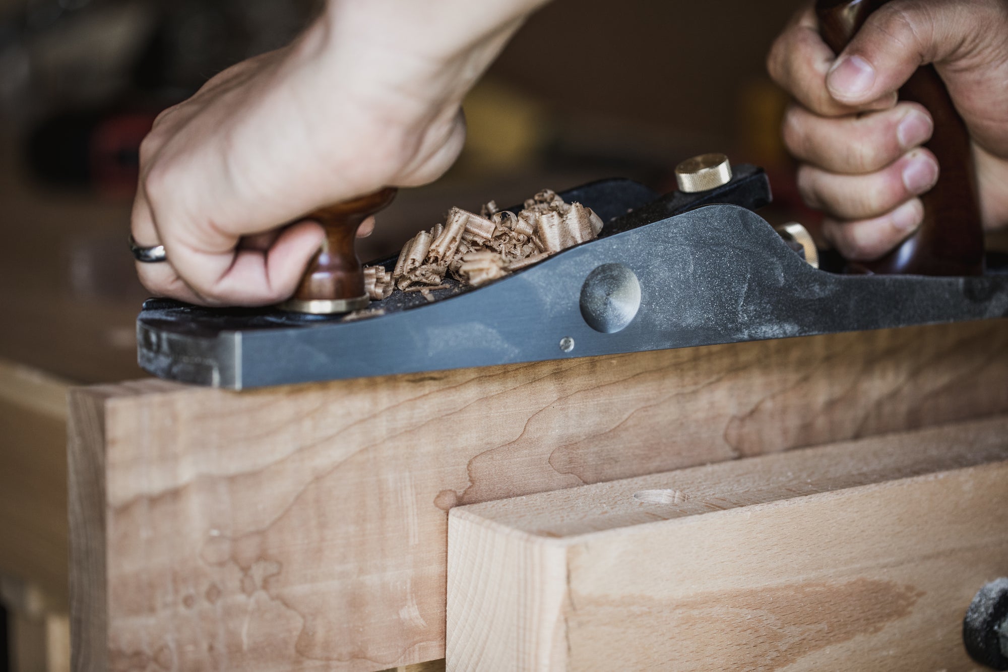 A close-up of hands using a hand planer on a piece of wood, demonstrating craftsmanship and woodworking skills.